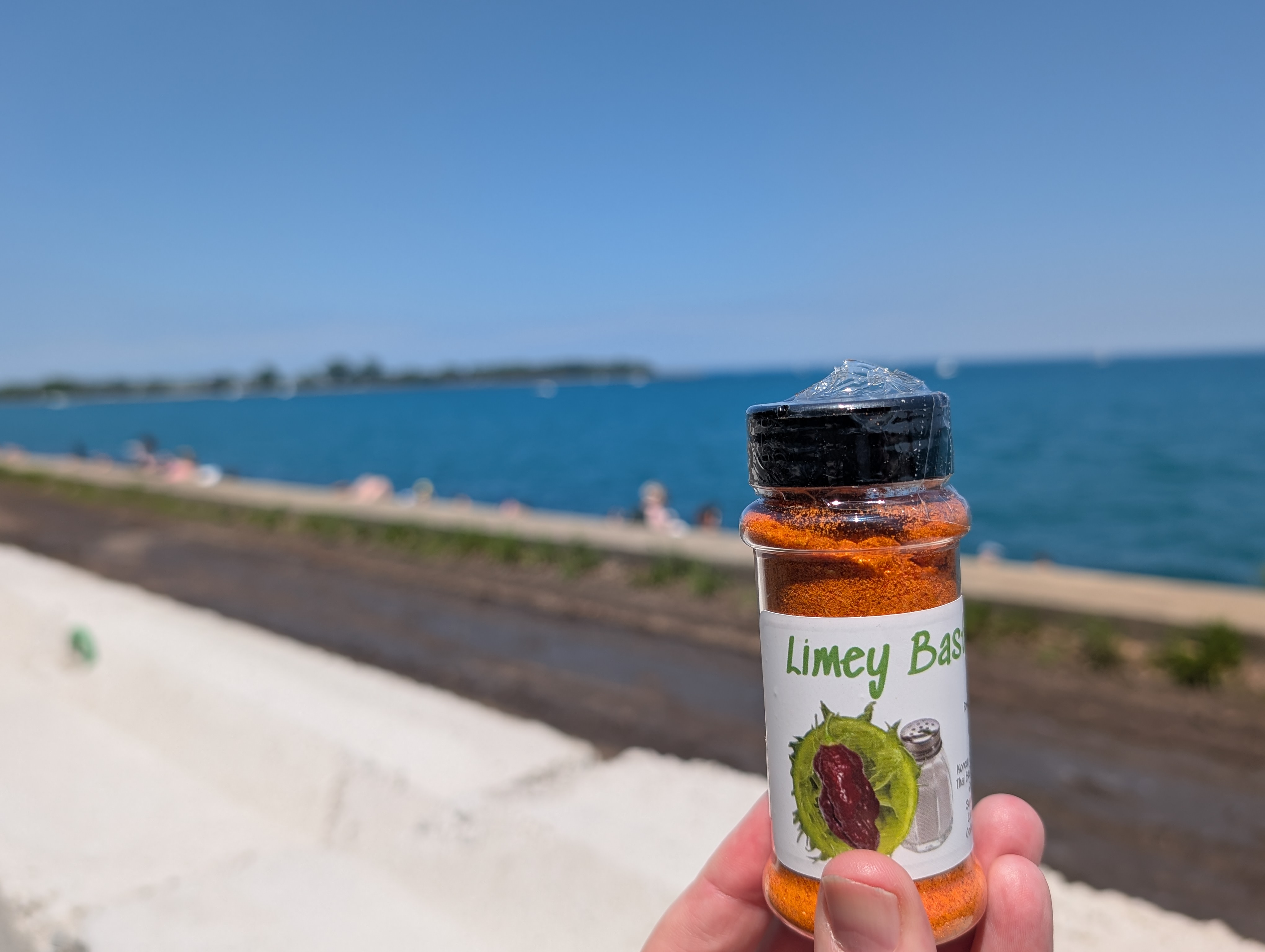 Hand holding a Limey Bastard spice jar by the water on a sunny day